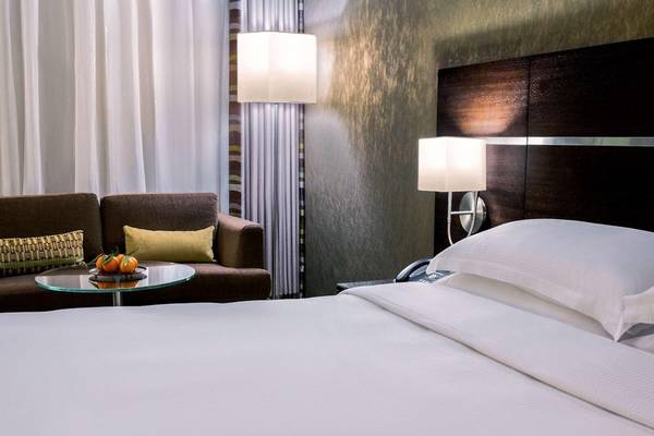 Hotelzimmer mit Bett, Couch, Tisch, Lampen und Obst auf dem Tisch.