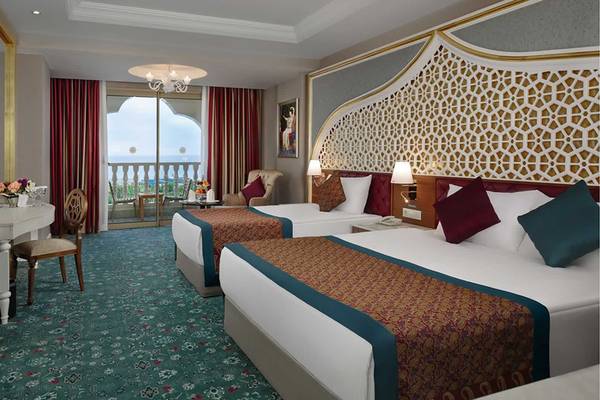 Innenansicht eines Hotelzimmers im Royal Taj Mahal Hotel mit zwei Betten, einem Fernseher, einem Tisch und einem Balkon