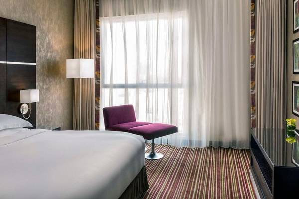 Schlafzimmer im Hyatt Regency Oryx Doha mit weißem Bett, violettem Stuhl und großen Fenstern.