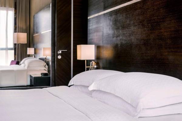 Schlafzimmer im Hyatt Regency Oryx Doha mit gemachtem Bett, weißen Laken und Kissen, sowie zwei Nachttischen und Lampen.
