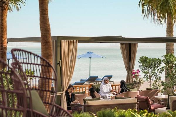 Außenbereich des Four Seasons Hotel Doha mit Gästen, die an Tischen sitzen und den Blick auf das Meer genießen.