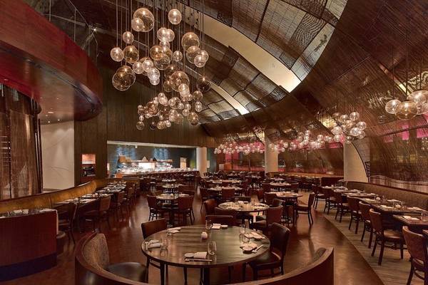 Innenbereich des Four Seasons Hotel Doha mit vielen runden Tischen und Stühlen, hängenden Lichtern und Holzboden.