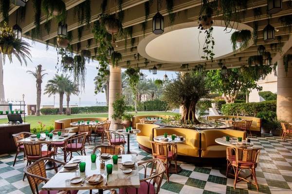 Terrasse des Four Seasons Hotel Doha mit gedeckten Tischen und Stühlen, umgeben von Pflanzen und Bäumen.