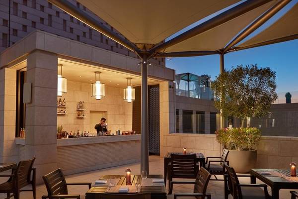 Außenbereich des Mandarin Oriental Doha Hotels mit Bar und Tischen unter einer Markise