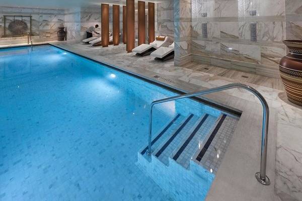 Innenpool des Mandarin Oriental Doha mit Marmorwänden und Duschen.