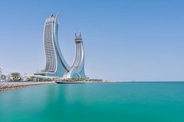 Außenansicht des Raffles Doha Hotels mit zwei geschwungenen Türmen und klarem Wasser im Vordergrund