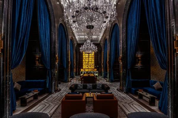 Lobby des Raffles Doha Hotels mit blauen Vorhängen, Kristallkronleuchtern und gepolsterten Möbeln.