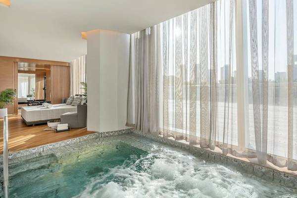 Ein eleganter Innenpool im Raffles Doha Hotel mit fließendem Wasser und einer Stadtansicht durch große Fenster.