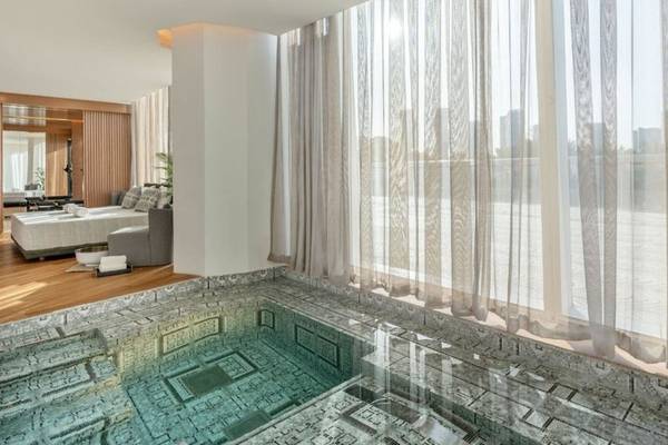 Innenpool im Raffles Doha Hotel neben einem Bett und großen Fenstern.