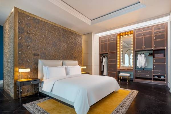 Schlafzimmer im Raffles Doha mit weißem Bett, Nachttischen, Lampen und einem großen Spiegel.