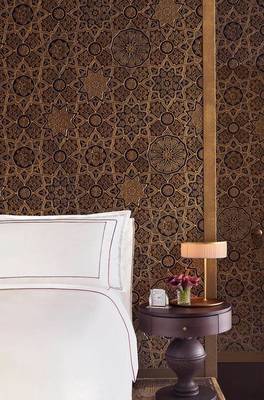 Schlafzimmer im Raffles Doha Hotel mit gemusterter Wand und Nachttisch.
