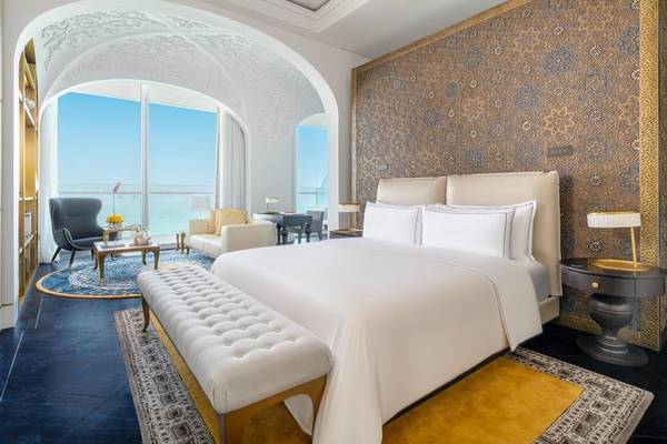 Schlafzimmer im Raffles Doha mit großem Bett, Blick auf den Ozean und eleganter Inneneinrichtung.