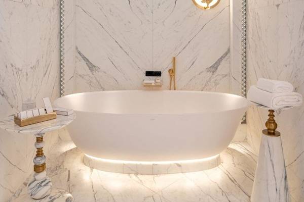 Badezimmer im Raffles Doha mit einer weißen Badewanne, Marmorwänden und goldenen Armaturen.