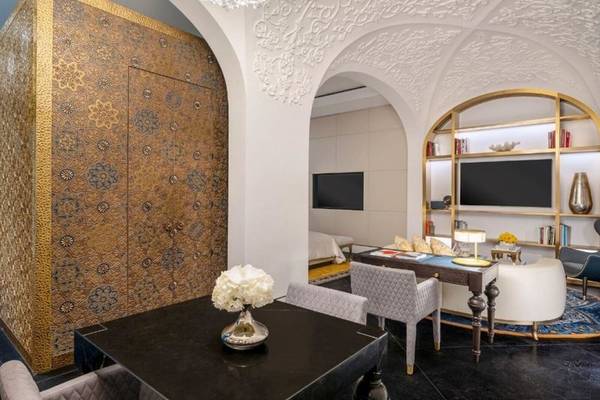 Inneneinrichtung der Raffles Doha Suite mit goldenen Wandverkleidungen, einem schwarzen Tisch mit einer Blumenvase, einem Schreibtisch, Sesseln und einem Fernseher.