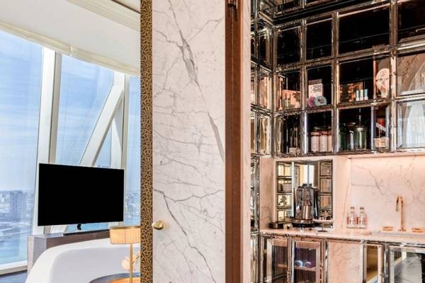 Innenansicht des Schlafzimmers im Raffles Doha Hotel mit Marmorwänden, einem großen Bett, Fernseher und Minibar.