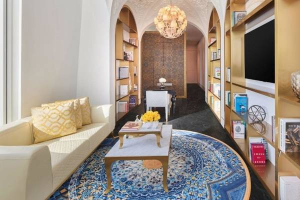 Innenansicht des Wohnzimmers im Raffles Doha mit weißem Sofa, goldenem Tisch, blauem Teppich und Bücherregalen.