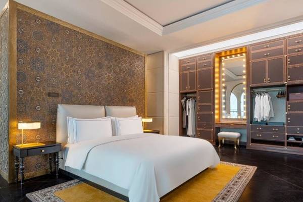 Innenansicht des Schlafzimmers im Raffles Doha Hotel mit einem großen Bett, Nachttischen und einem Kleiderschrank.