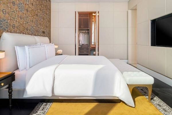 Schlafzimmer im Raffles Doha Hotel mit einem großen Bett, weißen Laken, Kissen und einem weißen Ottoman.
