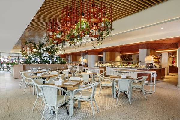 Innenbereich des Grand Park Lara Hotels mit geometrischen Mustern, Tischen und Stühlen, hängenden Pflanzen und einem Büffet.