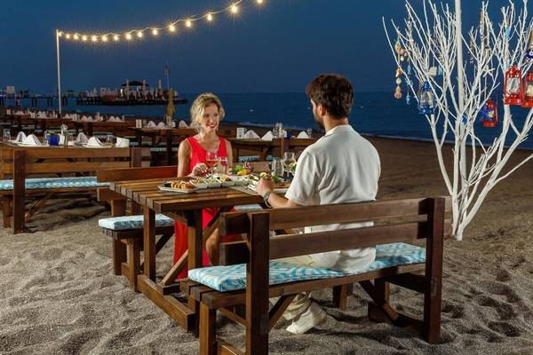 Paar isst am Tisch auf dem Strand des Grand Park Lara Hotels bei Nacht.