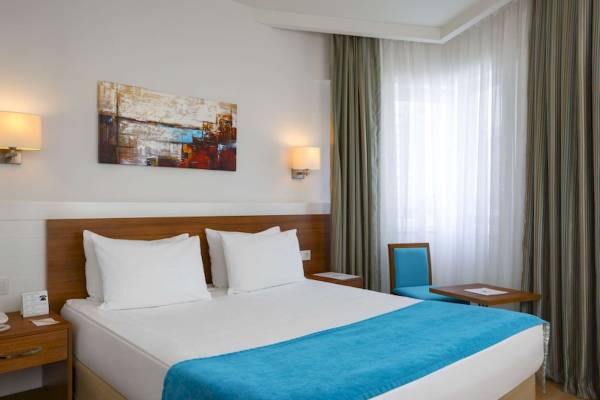 Schlafzimmer im Grand Park Lara Hotel mit einem Doppelbett, zwei weißen Kissen, blauer Decke, und einem blauen Stuhl neben einem Tisch.