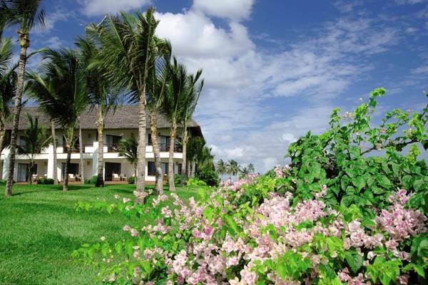 Außenansicht des Sea Cliff Resort & Spa mit weißen Gebäuden, Palmen und rosa Blumen.