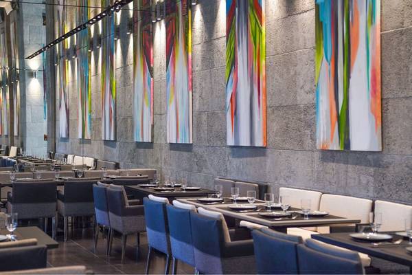 Innenraum des St. Regis Doha mit leeren Tischen, Stühlen und farbigen Wandgemälden.