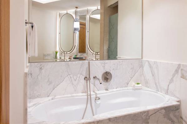 Badezimmer im St. Regis Doha mit Badewanne und Marmorwänden, Spiegeln und Glastür.