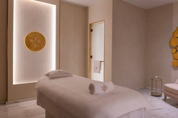 Massage-Behandlungsraum im St. Regis Doha mit weißem Bett, Kissen, Handtüchern und goldenem Wandschmuck.