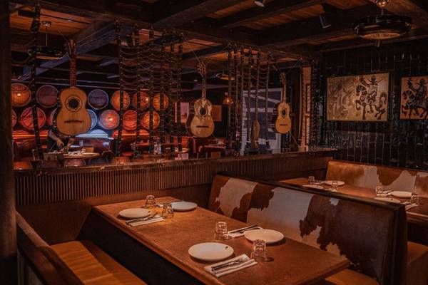 Innenraum des St. Regis Doha mit dunklen Wänden, Holzbänken, aufgehängten Gitarren und Gemälden.