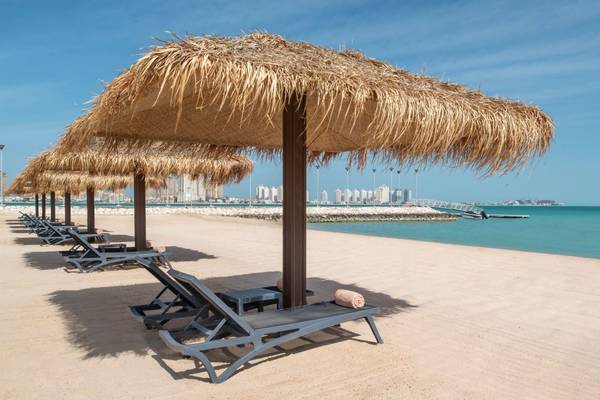 Strand am St. Regis Doha Hotel mit Sonnenliegen und Sonnenhüten
