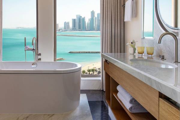 Badezimmer mit Meerblick im St. Regis Doha, mit Badewanne, Waschbecken und Stadtsilhouette im Hintergrund.