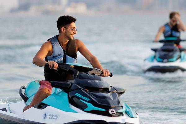 Zwei Personen auf Jetski im Wasser, eine vordere Person lächelt in die Kamera.