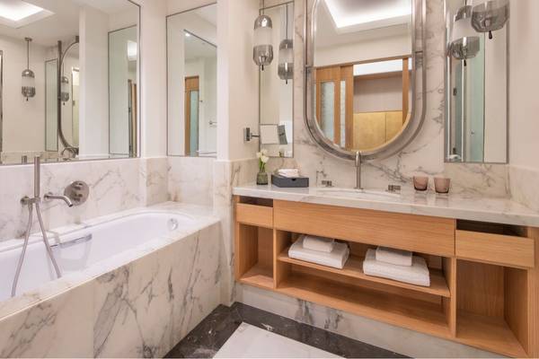 Das Badezimmer im St. Regis Doha Hotel mit Badewanne, Spiegeln und Holzmöbeln.