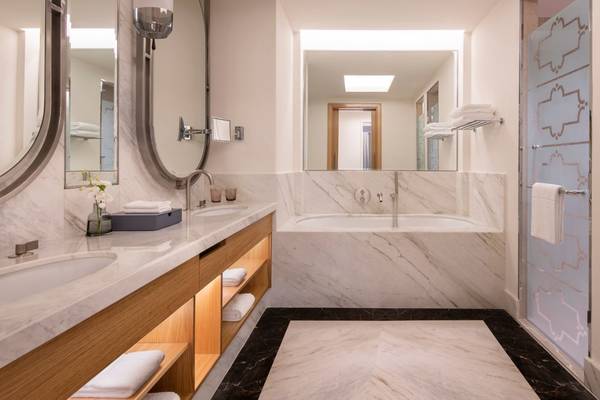 Innenansicht des Badezimmers im St. Regis Doha Hotel mit Marmorwänden und -böden, Badewanne, Waschbecken und Spiegeln.