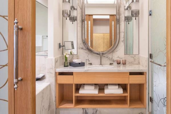 Badezimmer im St. Regis Doha mit Marmorboden, Waschbecken, Spiegel und Holzschränken.