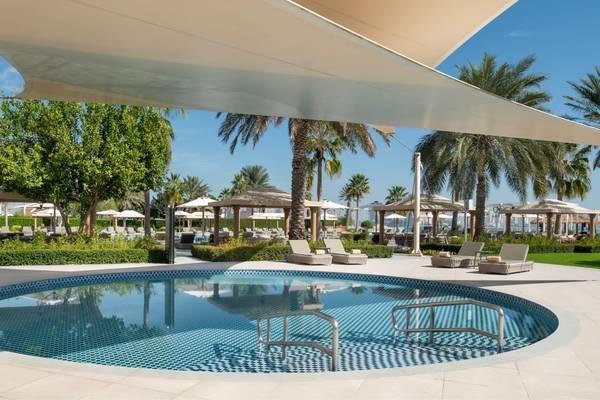 Poolbereich im Freien im St. Regis Doha Hotel mit Sonnenliegen und Schirmen.