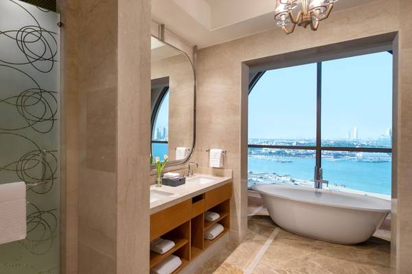 Das Badezimmer im St. Regis Doha mit Badewanne, Waschbecken und großer Fensterfront.