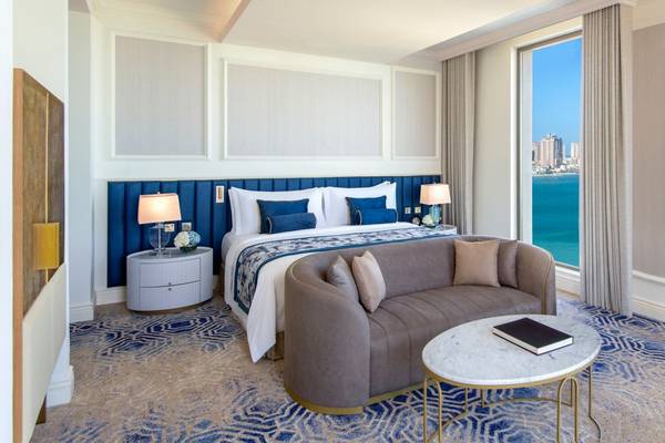 Innenansicht einer Suite im St. Regis Doha mit einem großen Bett, einem Sofa und einem Ausblick auf das Meer.