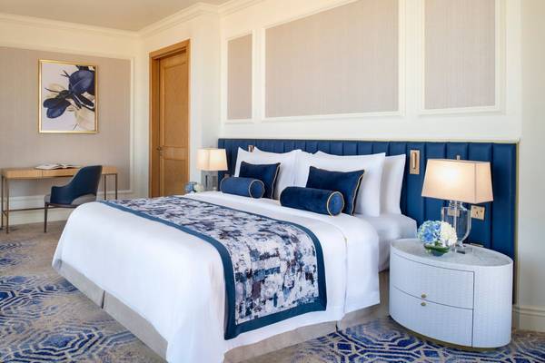Luxuriöses Schlafzimmer im St. Regis Doha mit blauen und weißen Kissen, einem großen Bett und einem Schreibtisch.