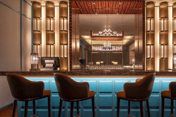 Innenansicht der Bar im St. Regis Doha mit blauen und goldenen Akzenten, drei Barhockern und einer Theke.