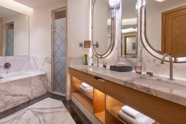 Luxus Badezimmer im St. Regis Doha mit Doppelwaschbecken, Badewanne und Marmorfliesen.