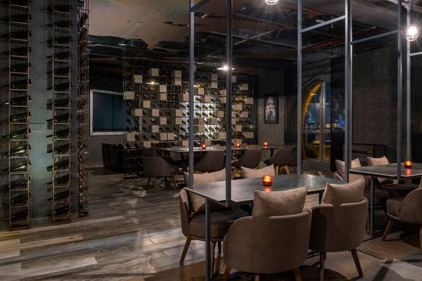 Innenansicht des Restaurants im St. Regis Doha mit runden Tischen und Stühlen, großen Fenstern und einer Weinflaschenwand.