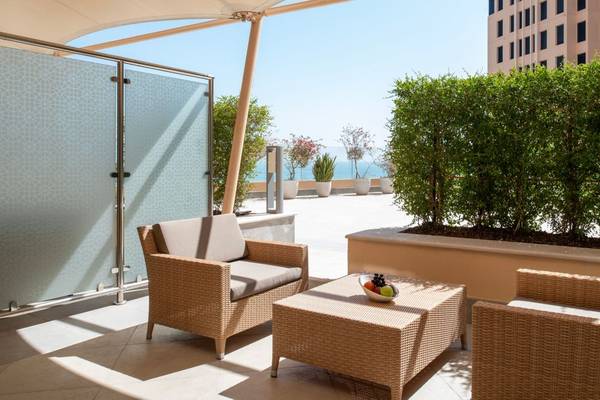 Balkon des St. Regis Doha mit zwei Rattanstühlen, einem Tisch und Blick auf das Meer.