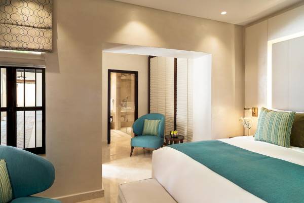 Zimmer im Souq Al Wakra Hotel mit Bett, Stuhl und Blick auf den Flur.