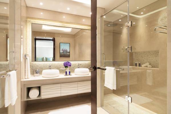 Badezimmer im Souq Al Wakra Hotel Qatar By Tivoli mit zwei Waschbecken und einer Glasdusche.