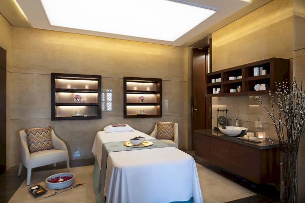 Spa-Behandlungsraum im Souq Al Wakra Hotel Qatar By Tivoli mit Massagetisch, Sesseln und Waschbecken.