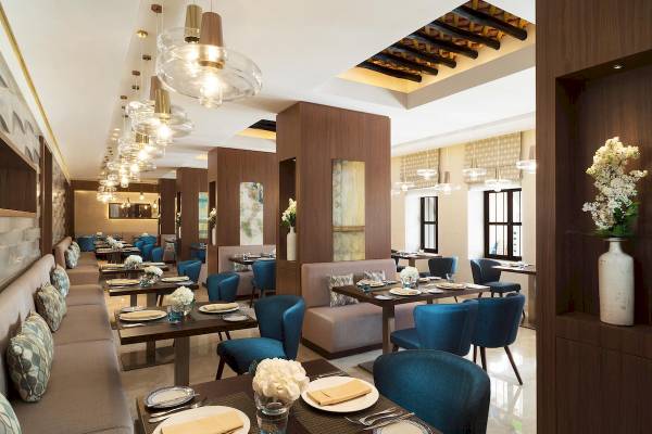 Innenansicht des Restaurants des Souq Al Wakra Hotel Qatar By Tivoli mit blauen Stühlen und Tischen.