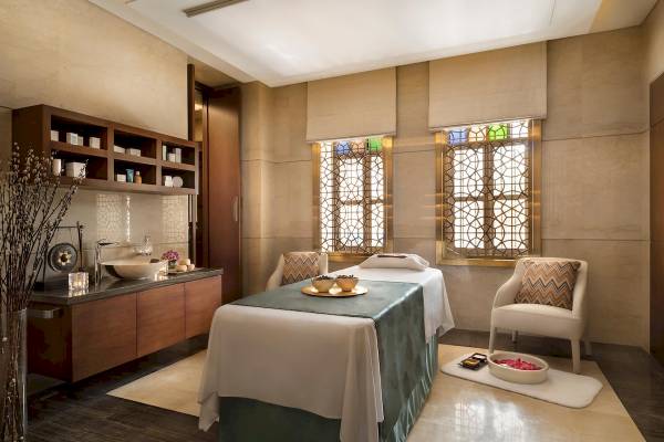 Spa Behandlungsraum im Souq Al Wakra Hotel Qatar By Tivoli mit Massageliege, Fenstern und Möbeln.
