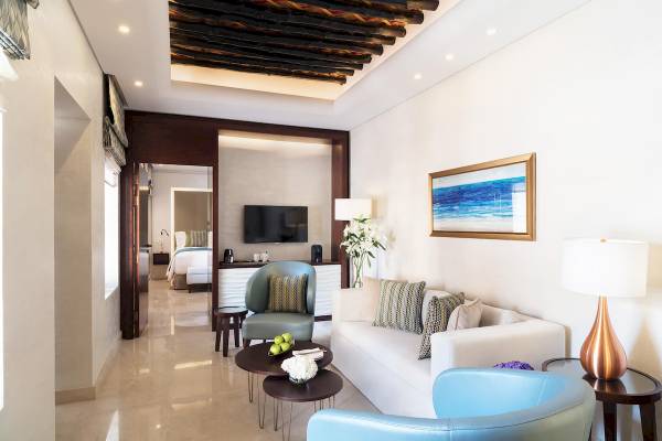 Innenansicht des Zimmers im Souq Al Wakra Hotel Qatar By Tivoli mit Couch, Sessel, Tisch, Fernseher und Gemälde.